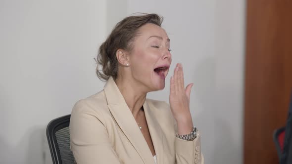 Tired Caucasian Beautiful Woman Yawning Sitting Indoors in Office