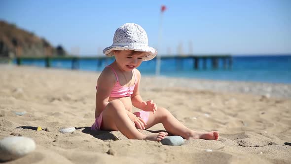 Little Girl in Pink Swimsuit Playing with Sand on the Beach