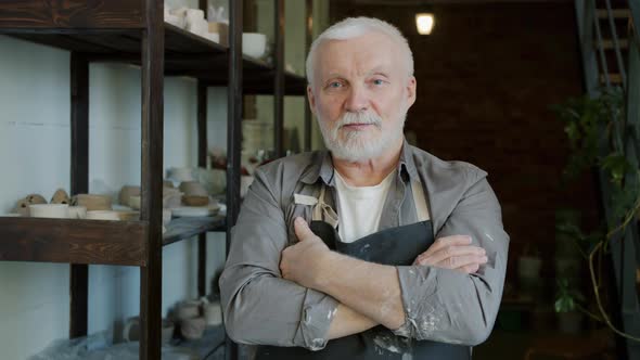 Portrait of Handsome Elderly Man Potter Standing in Workshop Wearing Apron and Looking at Camera