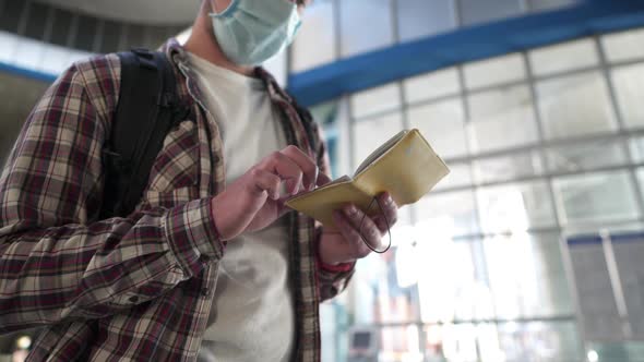 A Man with a Mask Takes Out a Passport and Tickets From His Pocket Watching the Departure Timetable