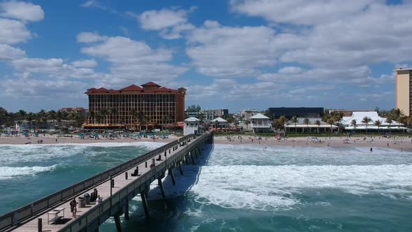 Aerial shot following waves breaking on the shoreline next to a pier