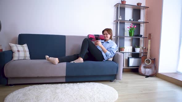 A woman lying on the couch uses a smartphone communicates via video communication greets the interlocutor