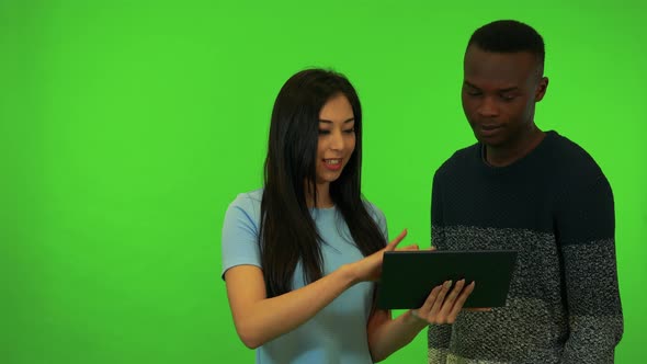 A Young Asian Woman and a Young Black Man Work on a Tablet Together - Green Screen Studio