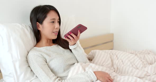 Woman sending audio message with smart phone and sitting on bed