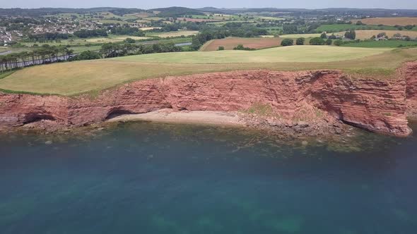 4K, Aerial Pull Back over the ocean past red sandstone cliffs along the Jurassic Coast in Devon