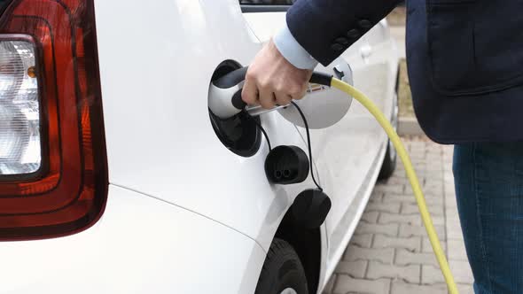 Man Coming to the Electric Car and Plugging in a Charging Cable