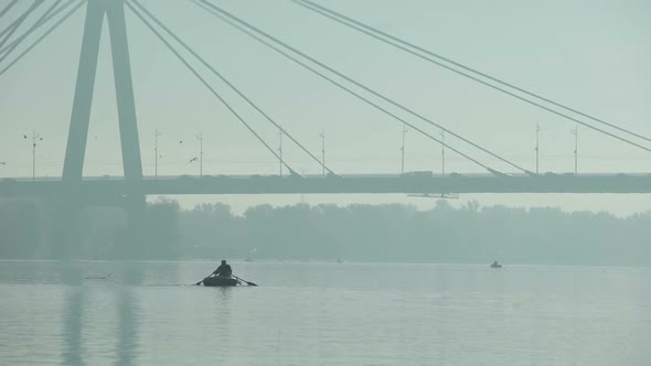 Fisherman Sailing Under Big Bridge on Inflatable Boat
