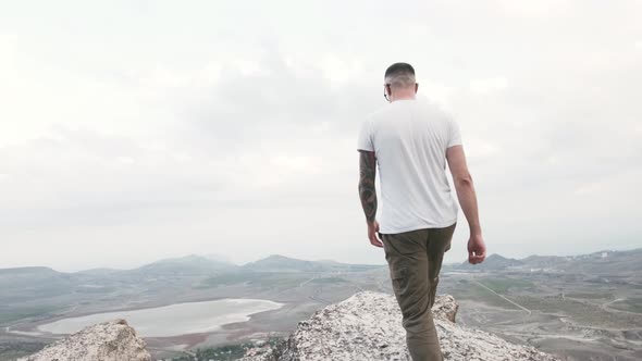 Happy Man Going on Top of Cliff and Raises Hands Up