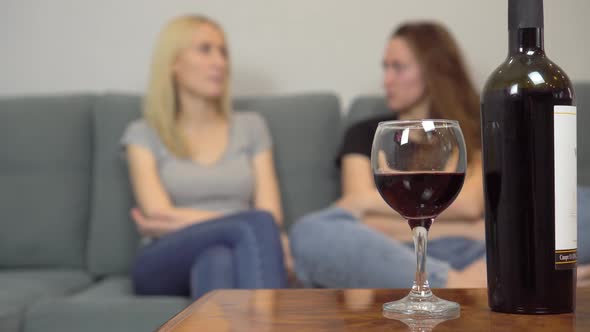 Two girls chat at home and drink red wine.
