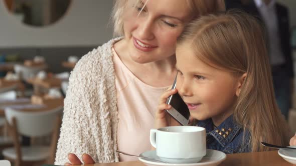 Little Girl Talks on the Phone at the Cafe