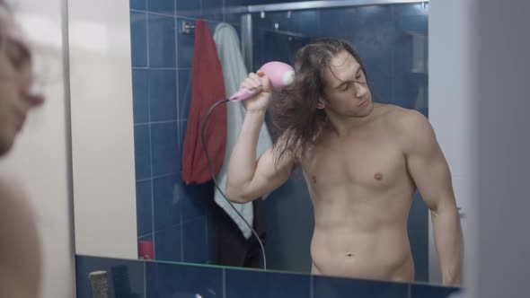 Completely Naked Metrosexual Man Using a Hair Dryer in Front of the Bathroom Mirror After a Shower