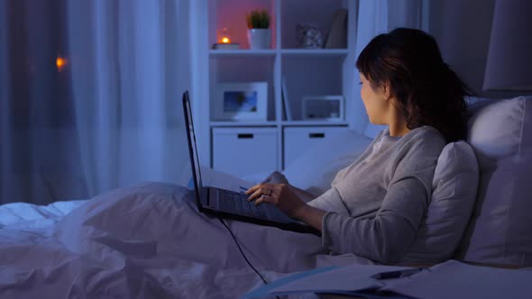 Woman with Laptop Working in Bed at Night