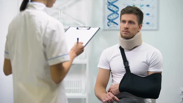 Doctor Writing Diagnosis to Upset Patient in Foam Cervical Collar and Arm Sling