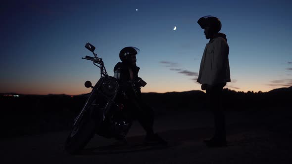 Silhouette Couple With Man Standing And Facing Woman Sitting On The Motorbike - wide shot
