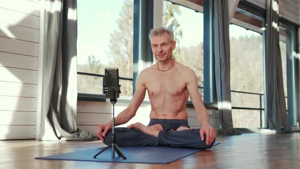 Mature Man Sitting Cross Legged on the Floor Doing Online Workout in Front of the Phone