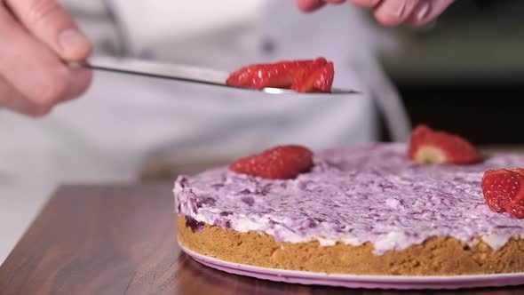 chef picks up sliced strawberries with knife and puts them prepared cheesecake.