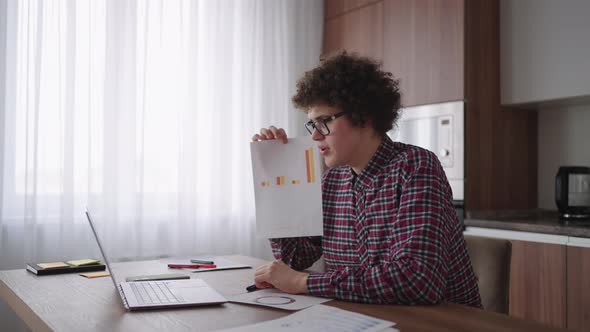 A Man with Glasses at the Table Shows a Picture with Graphs in the Camera of the Laptop