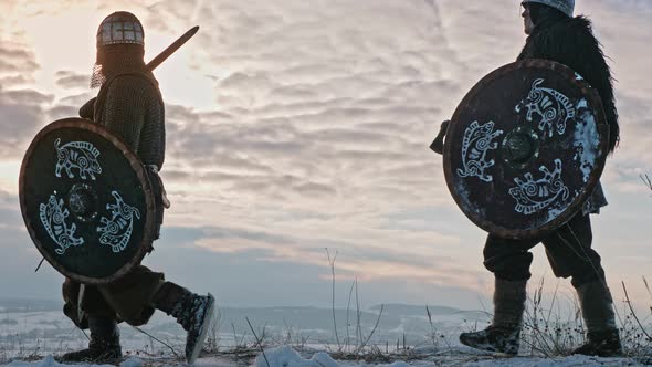 Group of medieval vikings with arms and shields going on the winter meadow alt