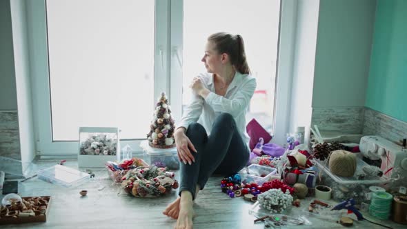 Girl is Sitting By Window Around Her Scattered for Christmas Decorations