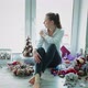 Girl is Sitting By Window Around Her Scattered for Christmas Decorations - VideoHive Item for Sale