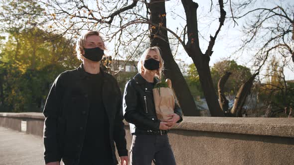 Portrait of Happy Young Couple in Protective Masks Walking Outdoors in Old City Center with Grocery