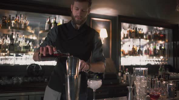 Bartender Pouring Alcohol in Beaker Then in Glass with Ice, Demonstrating His Skills