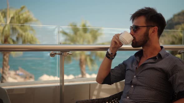 Businessman In Sunglasses. Businessman Drinking Tea On Vocation Resort. Man Sitting On Cafe Sea.