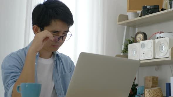 Young Asian businessman working on laptop at office, feeling tired and having headache.