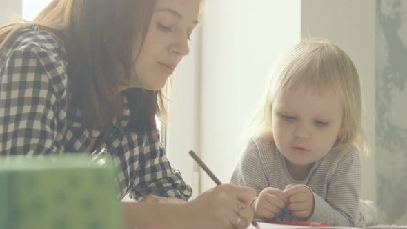 Mother and little daughter draws with pencils in album