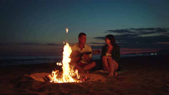 Pair sitting at campfire on beach