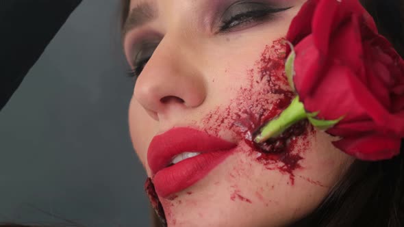 Glamorous Brunette Woman with Makeup for Halloween Rose Flower in Her Mouth