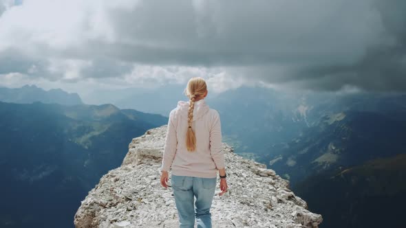 Back View of Blonde Woman Walking on the Top of the Mountain Under the Clouds