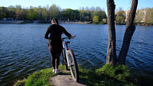 a woman with bicycle walking to lake, river in sunset time.