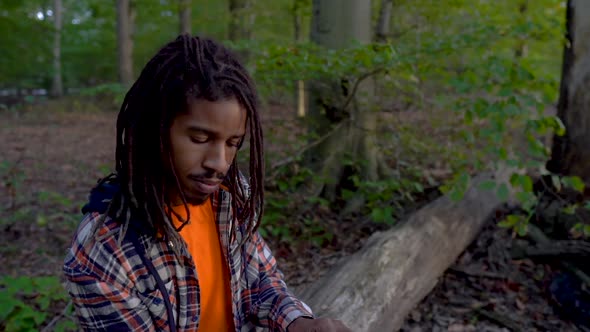 Young African American Man in the Park Reading a Book Surrounded By Nature