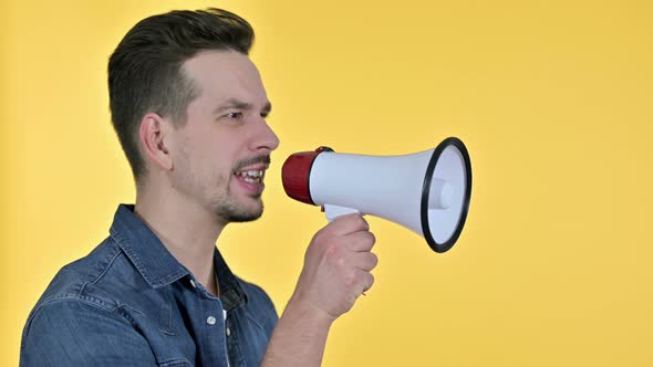 Portrait of Young Man Making Announcement on Loudspeaker, Yellow Background