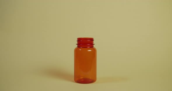 Slow motion wide shot of a single pill falling vertically towards a pill bottle, hitting the rim and