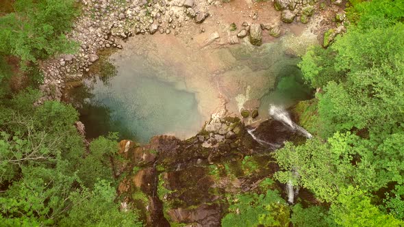 Aerial view of the top of a small waterfall with clean water downhill.