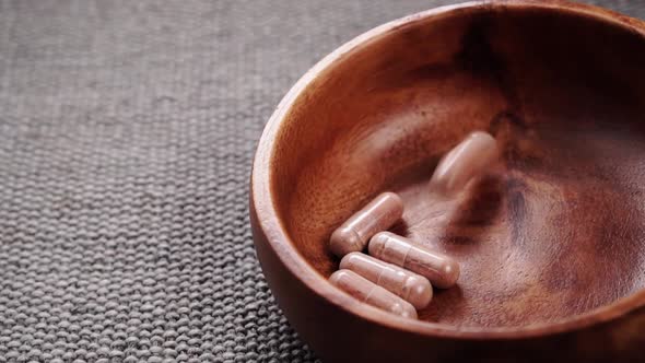 Medical herbal capsules fall into a rustic wooden bowl in slow motion. Close up