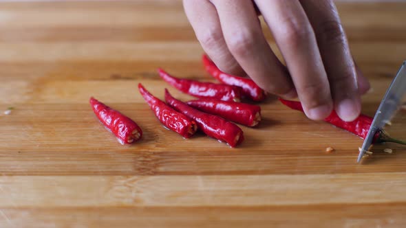 A Woman's Hands Chopping Red Chillies with Kitchen Knife on Wooden Cutting Board