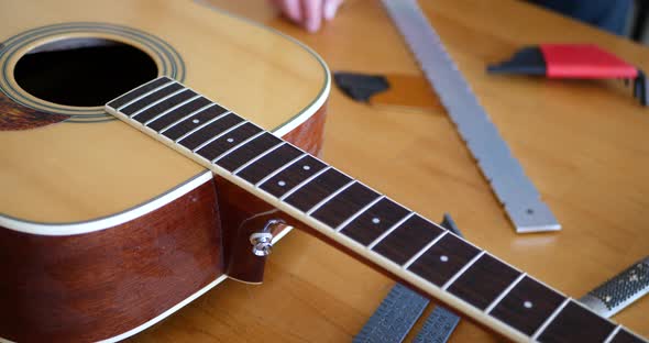Close up hands of a luthier craftsman measuring an acoustic guitar neck fretboard on a wood workshop