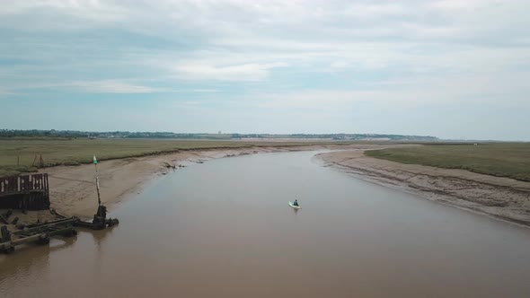 Man kayaking on meandering river, drone follows, beautiful landscape in the background