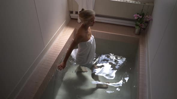 Steadicam shot of beautiful mature woman wearing towel and swirling water in historic Roman Bath in