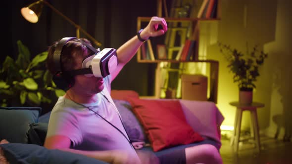 Young Man Wearing Virtual Reality Glasses and Headphones Playing Video Games Gamer Sitting on Sofa