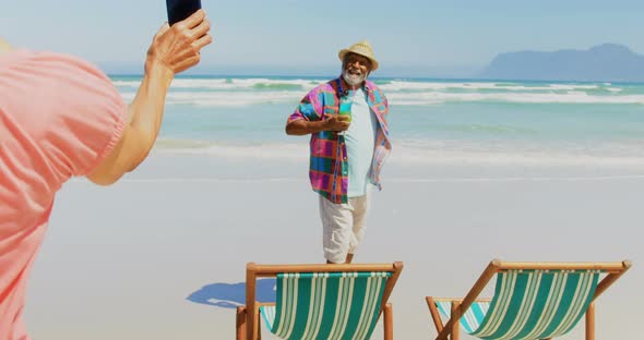 Rear view of active senior African American woman taking photo of man with mobile phone at beach 4k