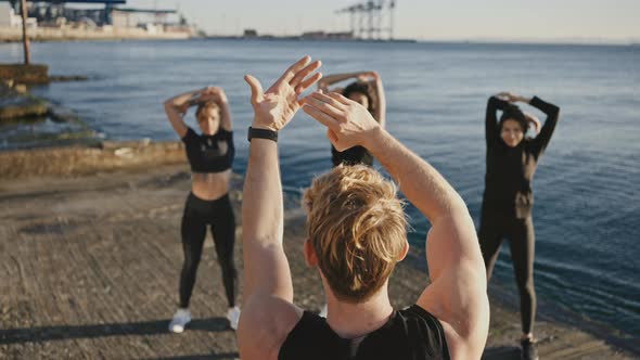 Three Diverse Women Practicing Workout at Seaside Repeating Exercises for Their Male Muscular Coach