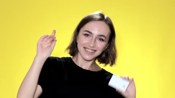 Smiling young woman holding credit card on yellow background.