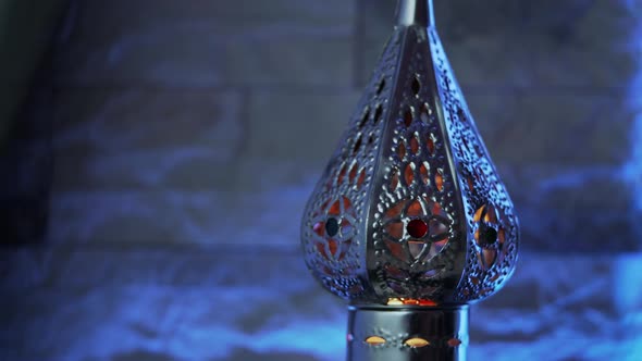 Oriental style lamp with burning candle rotating on light blue background