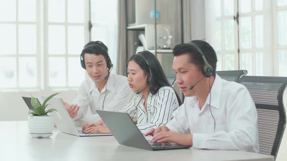 A Man Of Three Call Centre Agents Helping A Woman To Work With Computer While His Colleagues Working