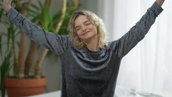 Medium Shot of Joyful Slim Smiling Woman Stretching in Bedroom at Home in the Morning