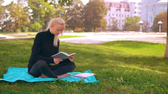Blond Girl Reads Book in Park